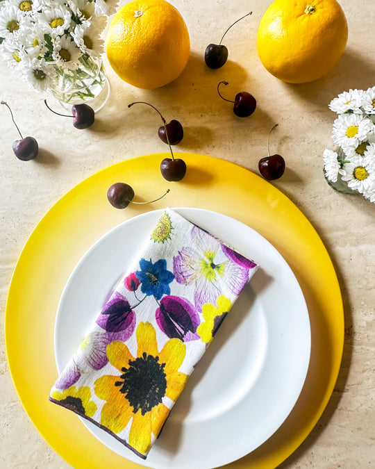 Floral printed napkin set by Tisch New York, displayed on a plate with citrus fruits. Set of four, 18x18 inches, pre-washed linen.