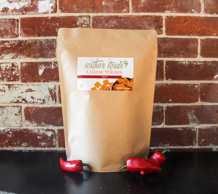 Southern Straws | Cheese Straws - Spicy flavor in a kraft pouch, with red chili peppers, showcasing crispy, spicy cheese snacks made from premium ingredients.