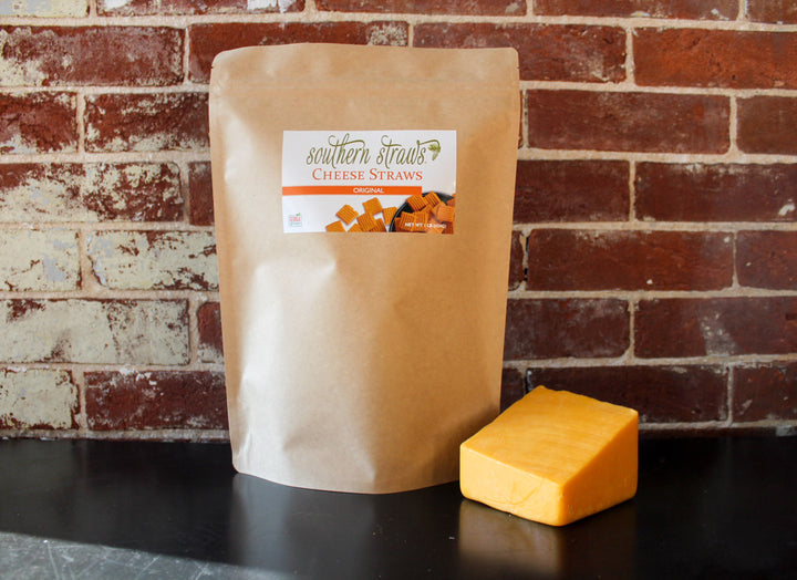 Southern Straws | Cheese Straws displayed beside cheddar block on a countertop, highlighting their artisanal, handcrafted recipe and classic Southern flavor.