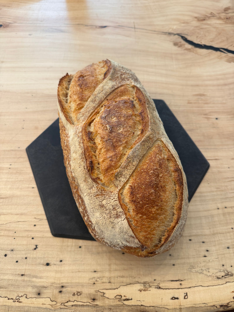 Independent Baking Co. | Sourdough loaf on dark serving board, showcasing its crusty, artisanal texture, perfect for enhancing culinary experiences from Athens Cooks.