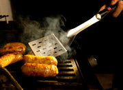 GrilLight | Gift Set - 2 Piece Spatula + Tongs shown grilling sausages, featuring LED lights for optimal evening cooking. Ideal for barbecue enthusiasts.