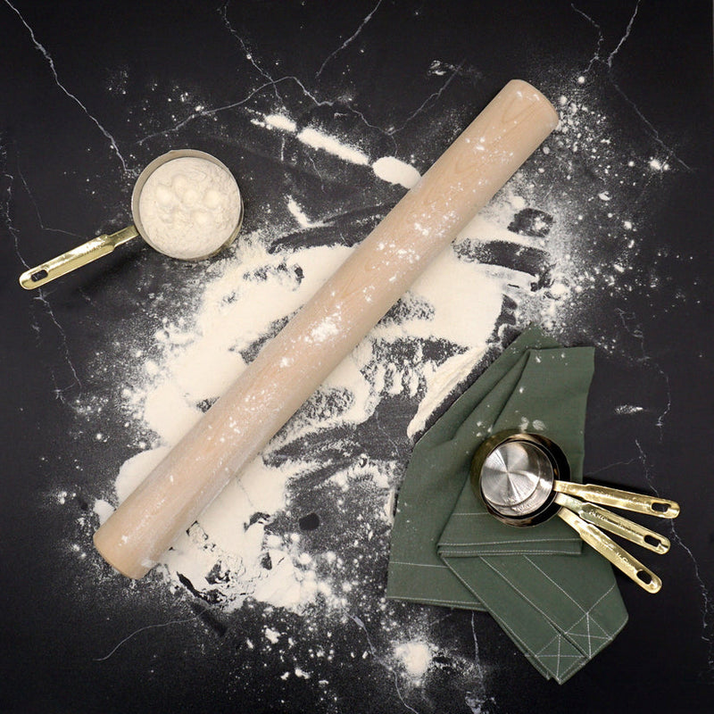 J.K. Adams | Plain Dowel Rolling Pin on flour-dusted countertop with brass and metallic measuring cups, highlighting its classic design and utility for baking tasks.