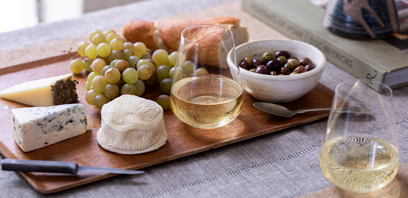 Richard Brendon | Jancis Robinson Stemless Wine & Water Glass Set of 2 alongside cheese, olives, and a glass of white wine on a table.