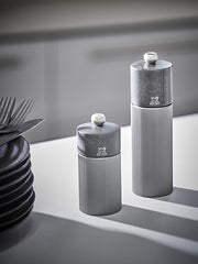 Peugeot | Line Pepper Mill, Aluminum + Beechwood, Carbon Finish, 7 inches, displayed on a countertop beside dark plates and forks, showcasing modern design and functionality.