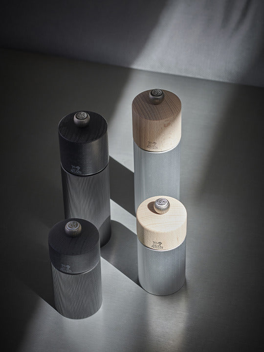 Peugeot | Line Pepper Mill, Aluminum + Beechwood, Carbon Finish, 7 inches, featuring ribbed metal bodies and turned-wood caps, exemplifying French craftsmanship with adjustable grind settings.