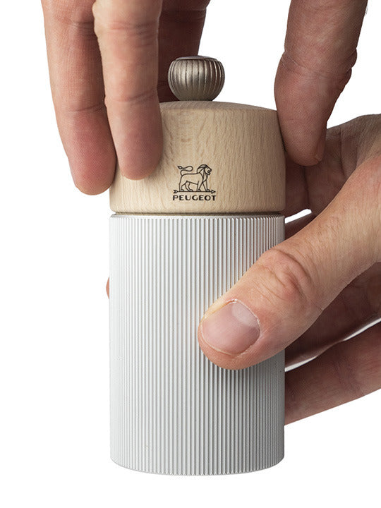 Peugeot | Line Pepper Mill Aluminum + Beechwood, Natural, 4.75 Inches, with a wooden top and ribbed aluminum body, held by hands, showcasing its adjustable grind setting.