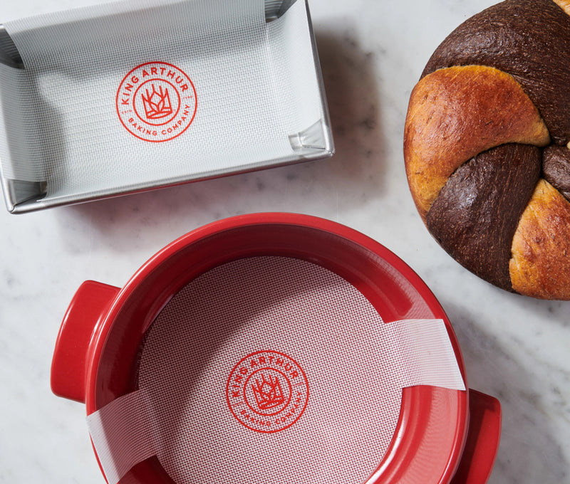 King Arthur Baking Company | Round Loaf Lifter in use, positioned beneath a fresh bread loaf, showcasing its nonstick utility for easy Dutch oven transfers.