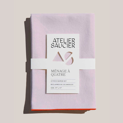 Atelier Saucier | Blush Linen Orange Napkins, Set of 4: Soft, neatly folded, pale-pink napkins with bright orange edges, wrapped in branded paper band.