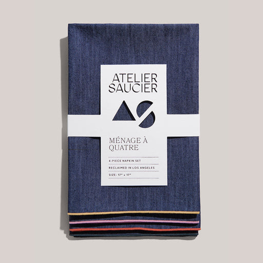 Atelier Saucier | Rainbow Denim Napkins, Set of 4, featuring dark-denim fabric with colorful piped edges, wrapped in a branded band, adding flair to dining.
