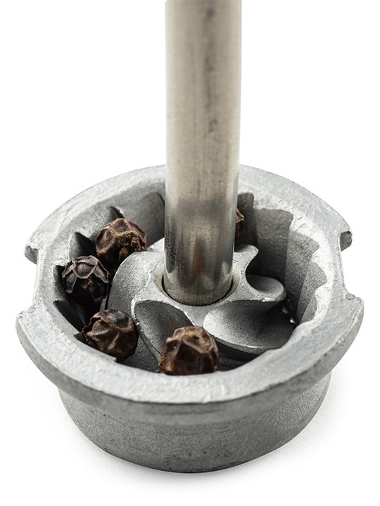 Close-up of Peugeot Bistro Pepper Mill's blade-guard, highlighting whole black peppercorns inside, illustrating its iconic French design and durable steel mechanism.