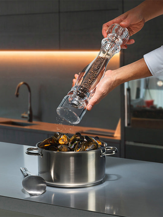 Peugeot | Paris Nancy Pepper Mill, Acrylic, 9 inches, seasoning a pot of mussels in a modern kitchen, highlighting its transparent design and adjustable coarseness feature.