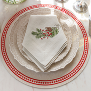 Natale Sprig Napkin in cream with embroidered pine branch, red berries, and pine cone, elegantly set in a festive winter tablescape.