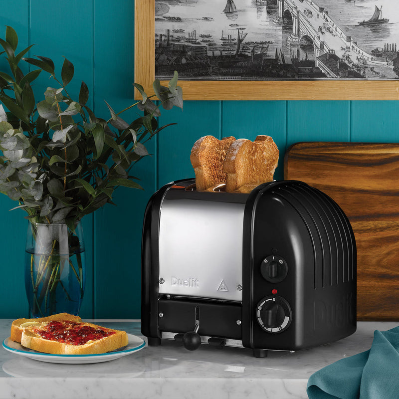 Dualit | 2 Slice Classic Toaster, Matt Black, with ProHeat ® elements, toasts bread on a countertop near jam-topped bread and leafy greens in an Athens Cooks kitchen scene.
