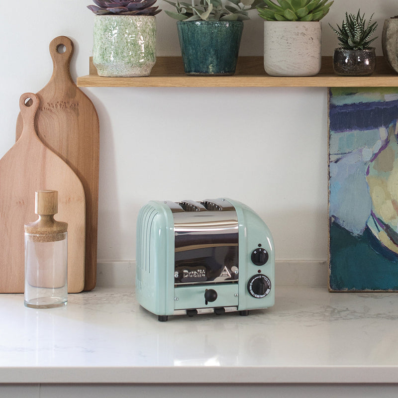 Dualit | 2 Slice Classic Toaster, Eucalyptus, with chrome accents on a white kitchen counter, surrounded by cutting boards and succulents at Athens Cooks.