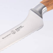 Close-up of Messermeister Oliva Elite Scalloped Offset Knife, showcasing the serrated stainless-steel blade and ergonomic olive wood handle, perfect for slicing bread effortlessly.