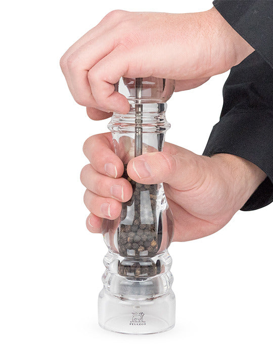 Peugeot | Paris Nancy Pepper Mill, Acrylic, 9 inches, showcased with peppercorns, being held and twisted to grind, highlighting its elegant design and adjustable coarseness knob.