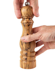 Peugeot | Paris Classic Olive Pepper Mill, Olive Wood, 9 inches, held and adjusted by hands, showcasing its elegant olive wood grain and functional metal knob.