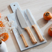 Opinel | Parallele Trio Chef Knife Set with olive wood handles displayed on a marble cutting board, surrounded by persimmons. Ideal for affordable kitchen upgrades.