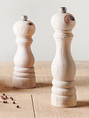 Peugeot | Paris Nature Collection Salt Mill, Nature, crafted from upcycled beech wood, stands elegantly on a wooden surface, accompanied by scattered peppercorns.