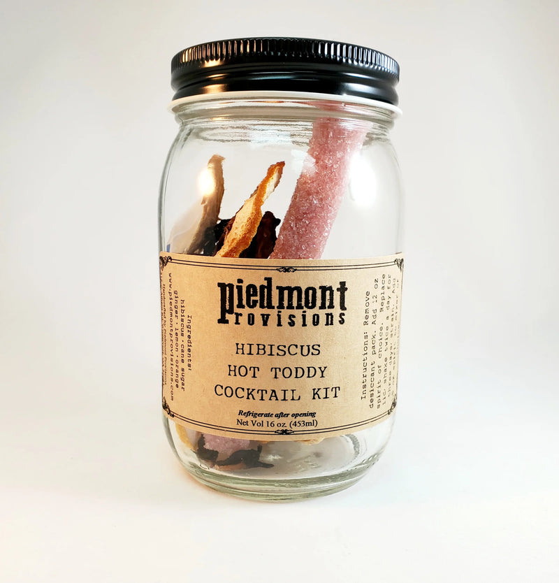 Piedmont Provisions Hibiscus Hot Toddy Cocktail Infusion Kit in a 16 oz glass jar with candy stirrer, dried hibiscus, and citrus peels.