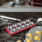 Marcato Ravioli Tablet on floured surface with freshly formed ravioli; includes rolling pin and mold for crafting ten perfect ravioli at once, ideal for home cooking.