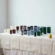 Sir|Madam Empire Footed Tuxedo Ale Glasses, Set of 2, displayed on a textured cloth with a row of various vessels and a solitary yellow fruit.