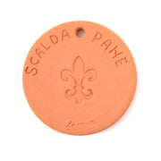Close-up of the UASHMAMA Scaldapane bread warmer, a round terracotta plate with a fleur-de-lis engraving, designed to keep bread warm in tabletop bags.