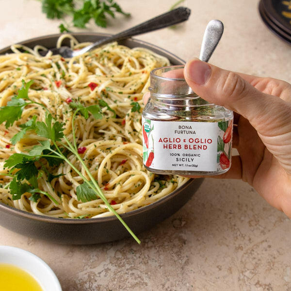 Bona Furtuna | Sicilian Seasonings - Mama Rose's Herb Blend jar held over a bowl of spaghetti, showcasing its use in enhancing Italian dishes.