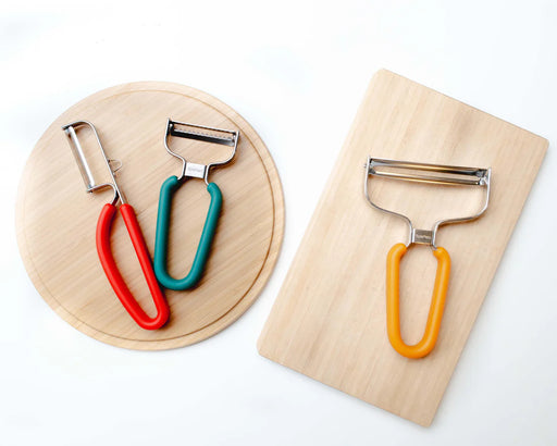 Spartan Kitchen Collection Box: Three versatile peelers on wooden boards, featuring stainless-steel blades and vibrant handles for efficient slicing, shredding, and peeling tasks.