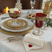 Arte Italica & Crown Linen Designs' Vetro Gold Charger elegantly complements a table setting with gold-trimmed plates, ornate glassware, and silver flatware, showcasing Tuscan craftsmanship.