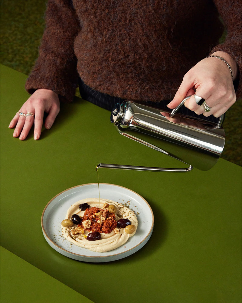 Holcomb Studio Oil Can pouring olive oil onto a plate of food, showcasing its elongated spout and sleek stainless steel design.