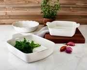 Emile Henry | Cheese Fondue Set in Burgundy sits among ceramic baking dishes and herbs on a kitchen countertop, showcasing its elegant, traditional design.