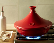 Emile Henry Deep Tart Dish, Clay, 2.1 QT, on a stove beside a wooden spoon and oil cruet, showcasing its robust ceramic design for culinary creations.