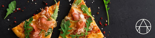 Two prosciutto and arugula pizza slices on slate, showcasing toppings and techniques for the Handmade Ravioli & Brown Butter Night cooking class at Athens Cooks.