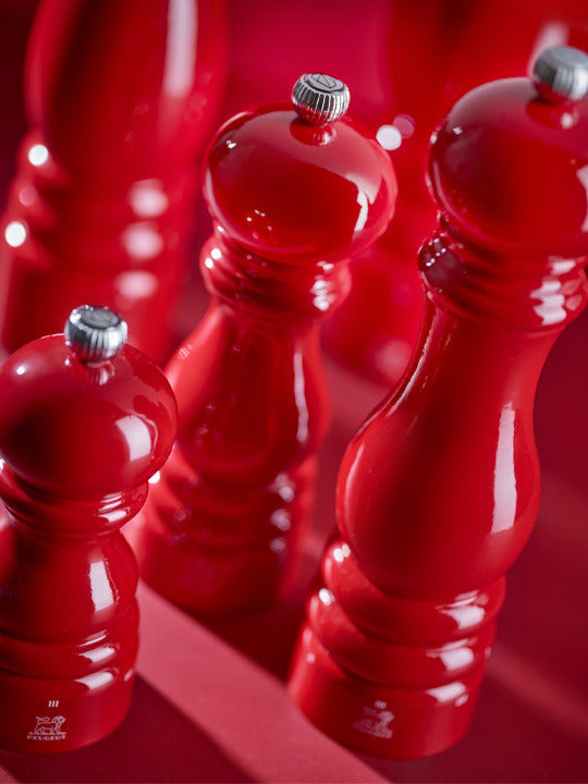 Peugeot | Paris Chef u'Select Passion Red Pepper Mill, 9 inches, with silver adjustment knob, classic hand-turned style, featured in a grouping against a red background.