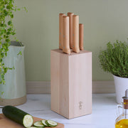 Opinel | 5-Slot Beech Wood Knife Block with light-wood handles, holding five knives, sits on a kitchen countertop beside a cucumber, herb plant, and olive oil.