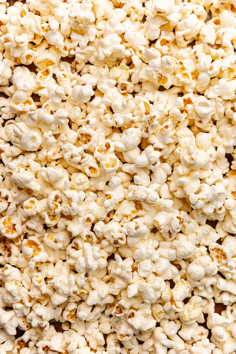 Poppy | Handcrafted Popcorns - White Cheddar: A close-up image of a pile of cheesy, gluten-free popcorn, perfect for snacking during game nights or movie outings.