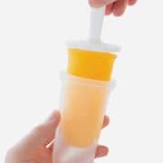 Hand holding a Zoku Classic Pop Mold filled with orange juice, illustrating its use for creating homemade popsicles, available at Athens Cooks.