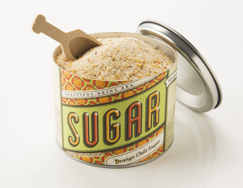 Beautiful Briny Sea - Orange Chili Sugar in a tin with lid off, revealing coarse sugar flecked with chili and citrus peel, and a wooden scoop.