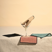 ATELIER SAUCIER - Luxxe Cocktail Napkins | Set of 4 displayed in a coupe glass, showcasing elegant, gold-spun fabric napkins bordered with black thread for a sophisticated touch.