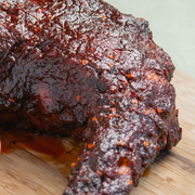 Beth's Farm Kitchen BBQ Sauce coats barbecued chicken, showcasing its glossy, reddish-brown finish, embodying a sweet, smoky flavor profile.