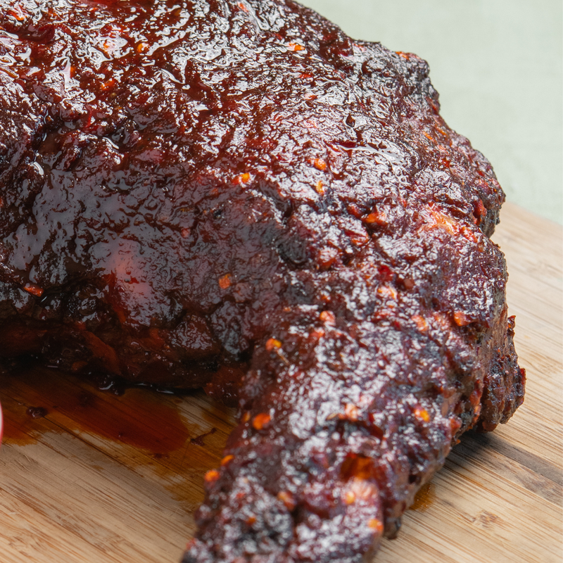 Beth's Farm Kitchen BBQ Sauce coats barbecued chicken, showcasing its glossy, reddish-brown finish, embodying a sweet, smoky flavor profile.