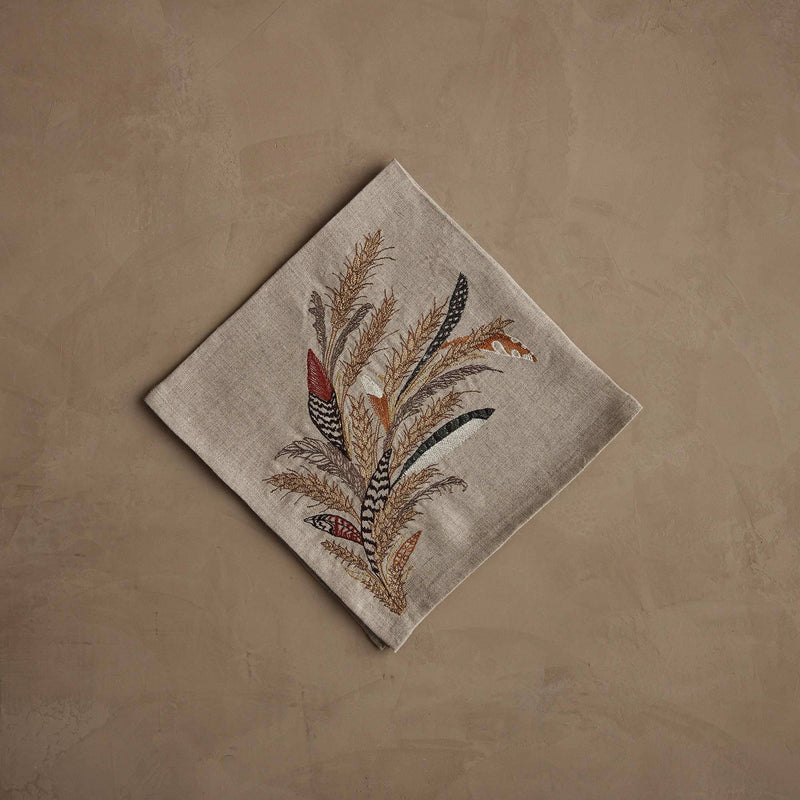 Coral & Tusk - Wheat Harvest Dinner Napkin features autumnal embroidery of feathers and grasses, set on natural linen, perfect for a bountiful fall table. Measures 20 × 20.