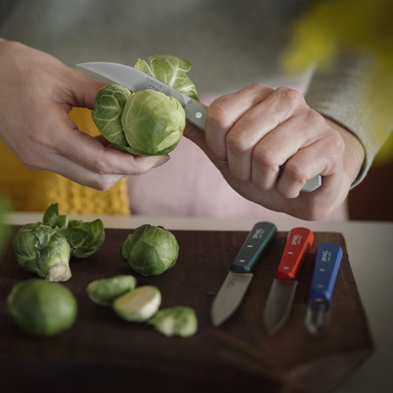 Person trimming Brussels sprout with Opinel knife from Opinel | Essential Small Kitchen Knife Sets Landscape; other knives and peeled sprouts on cutting board.