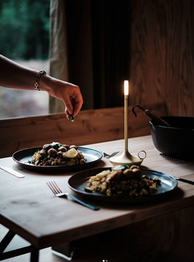 VANMOKUM | GRAYPANTS Wick Portable Rechargeable Lamp - Black on a dining table, enhancing ambiance with its candle-like glow amidst tableware and food.