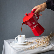 Bialetti | Red Moka Express Exclusive 3 Cup pours coffee into a white cup, showcasing its vintage-inspired design and modern elegance, perfect for coffee enthusiasts.