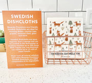 Bespoke Provisions - Cherries Swedish Dishcloth displayed in a basket with a descriptive sign, highlighting its eco-friendly, biodegradable features for kitchen cleaning.
