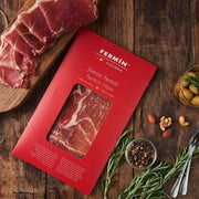 Casacella Foods - Fermin Serrano Ham Cured 18 Months 2 oz, elegantly displayed with sliced ham, nuts, olives, and rosemary, ideal for a charcuterie-style snack.