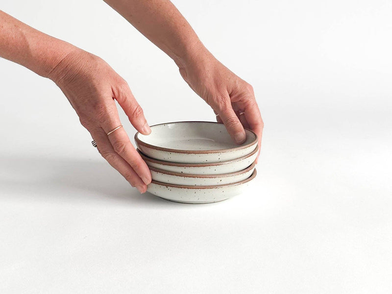 Sarah Kersten - Olive Dish: Basin Collection: Fig. A stack of white ceramic dishes, versatile for appetizers or sides, shown with a hand gently touching the top dish.