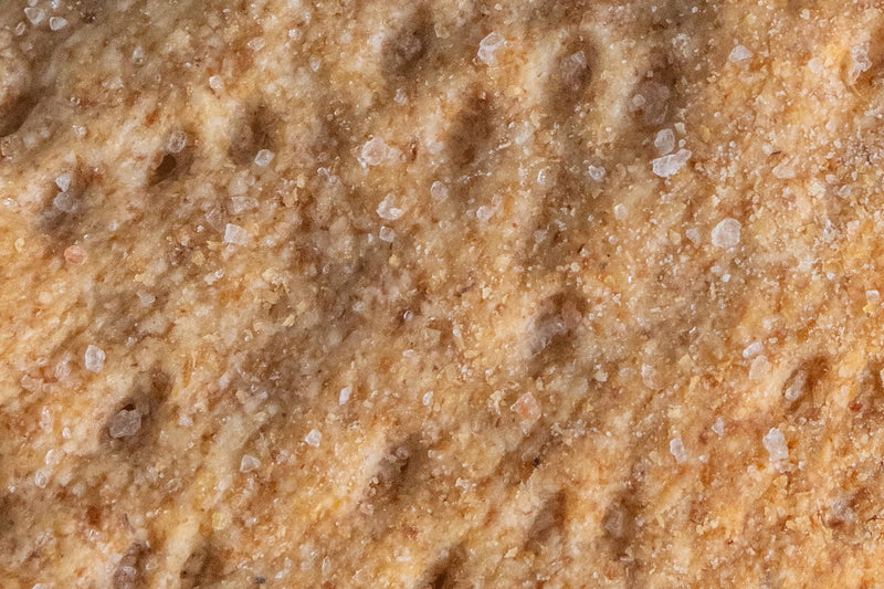 Close-up of Potters Table - Salted Olive Oil Flatbreads, showcasing their coarse salt-sprinkled surface, highlighting the artisanal texture and rustic appeal of these organic, hand-stretched crackers.